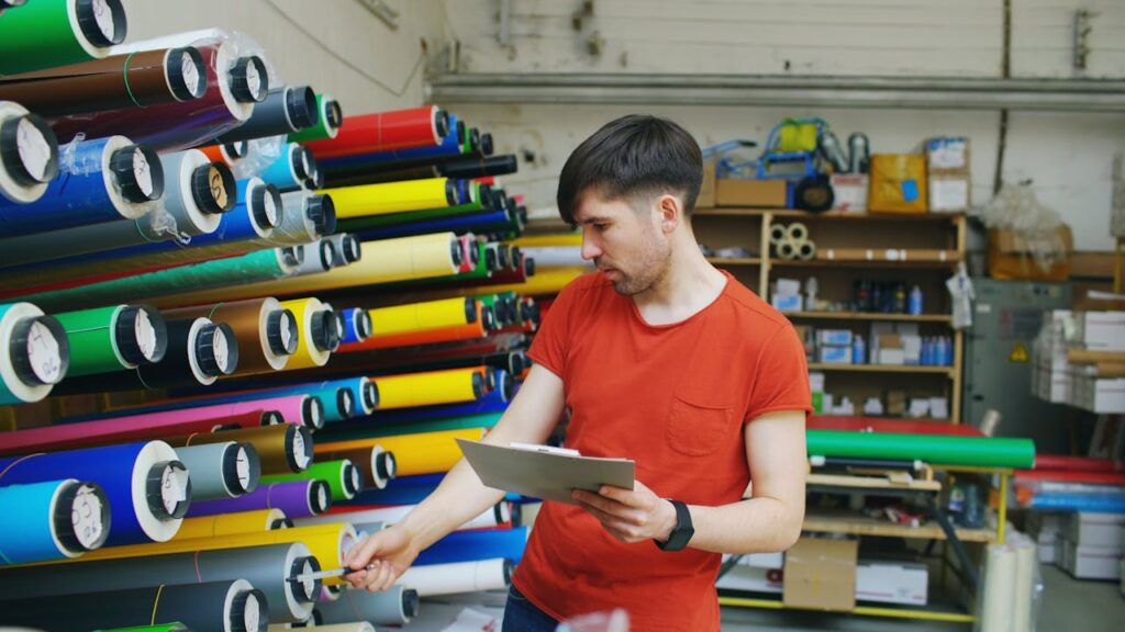 A man examining rolls of colorful vinyl in an industrial warehouse setting.